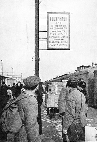 ARRIVAL IN MOSCOW. Travellers on a Moscow platform looking at a poster advertising a new railway hotel