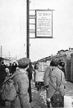 ARRIVAL IN MOSCOW. Travellers on a Moscow platform looking at a poster advertising a new railway hotel